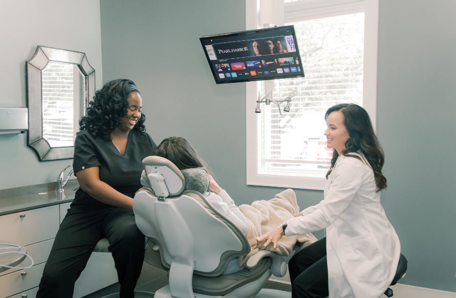 A dentist and team member sitting beside a patient in a dental chair