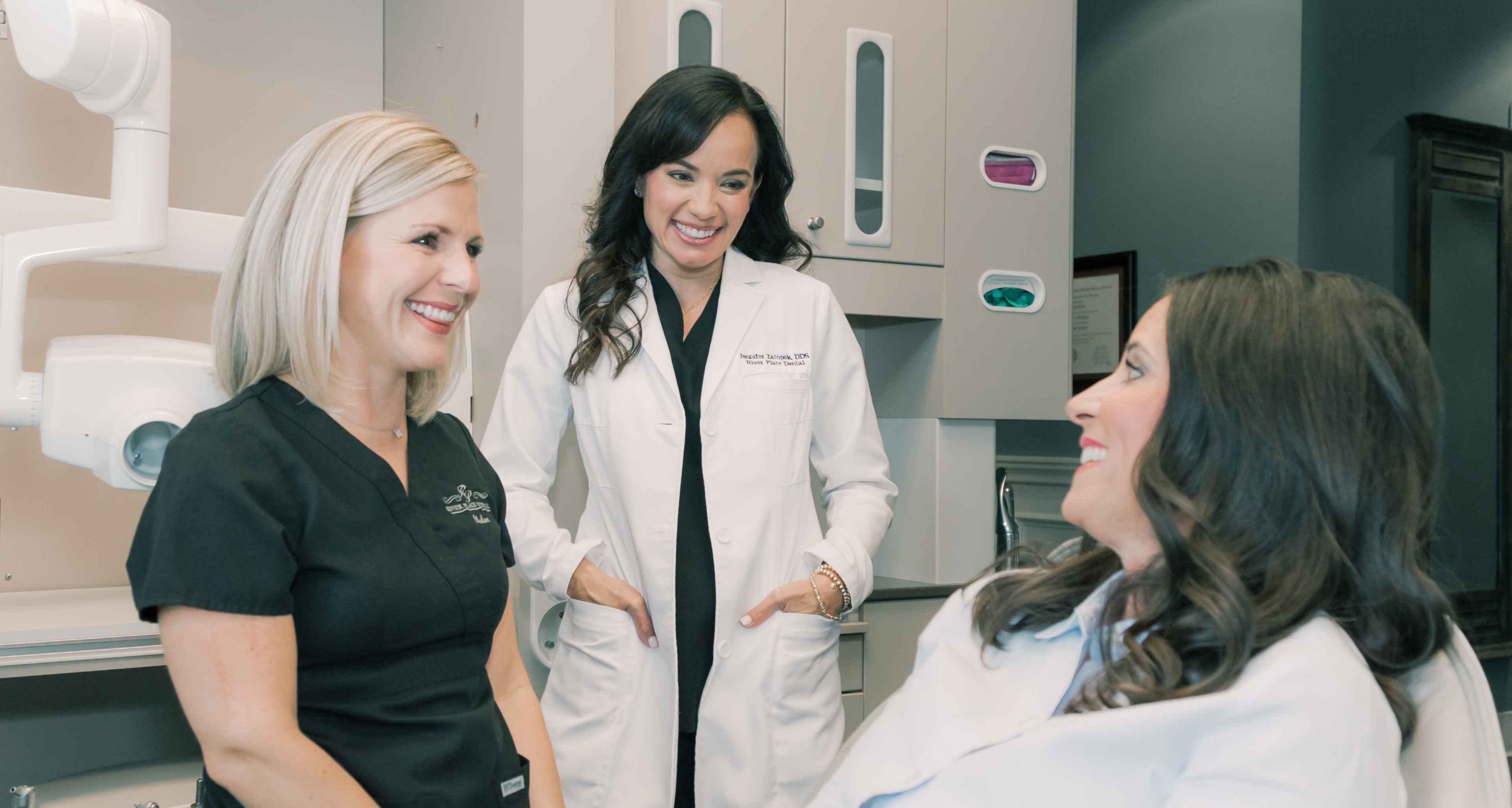 A dentist and team member talking with a smiling patient